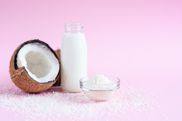 Coconut milk in the glass bottle, coconut flakes and fresh coconut on pink background.