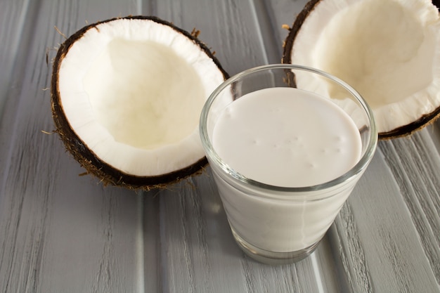 Coconut  milk in the glass and halves of coconut on the grey wooden  background