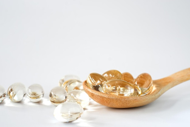 Coconut oil capsules in a wooden spoon on a white background. Health food supplement concept.