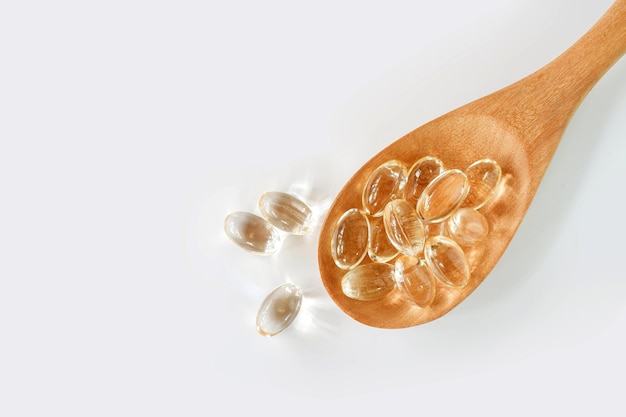 Coconut oil capsules in wooden spoon on white background, top view, Health food supplement concept.