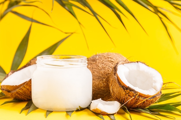 Coconut oil and coconuts on a background with tropical leaves