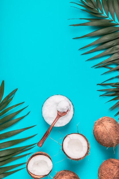 Coconut oil and coconuts on a with tropical leaves.