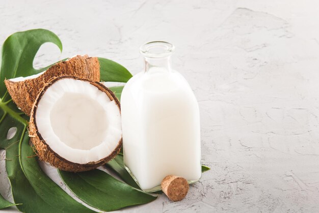 Olio di cocco in bottiglia di vetro con noce fresca e foglia di monstera