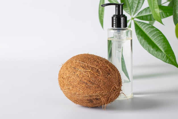 Foto olio di cocco in una bottiglia trasparente e cocco fresco su sfondo bianco prodotto cosmetico naturale per viso corpo e capelli copia spazio