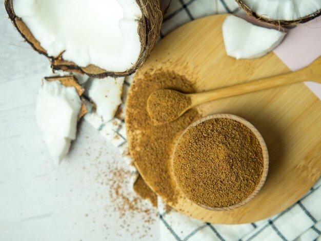 Coconut palm brown sugar in a wooden bowl and spoon and half of the coconut fruit on a gray concrete background