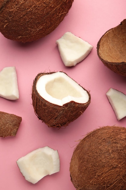 Coconut on a pink background. Halves and whole coconuts. Vertical photo.