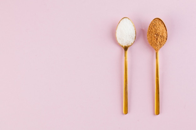 Photo coconut and refined white sugar in gold spoons on a pink surface