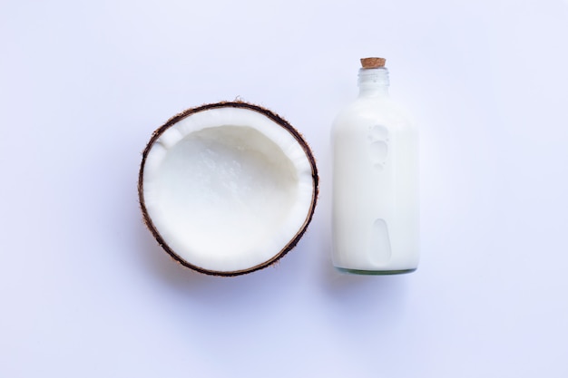 Noce di cocco con la bottiglia di latte di cocco su fondo bianco.