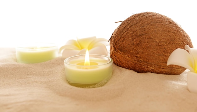 Coconut with plumeria and candles on sand isolated on white