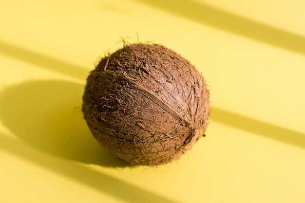 Coconut with shadows on yellow background. Tropical summer design. Creative concept.