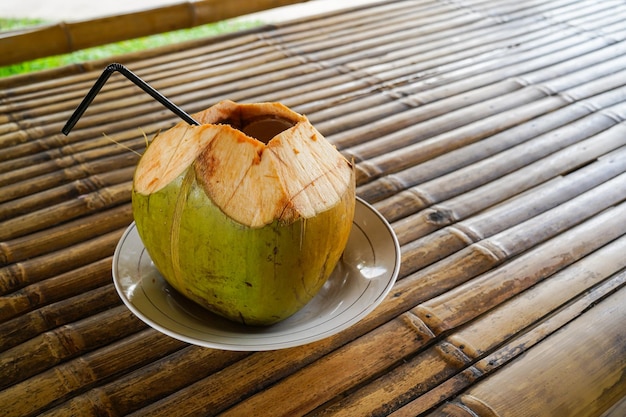 A coconut with a straw on a bamboo table