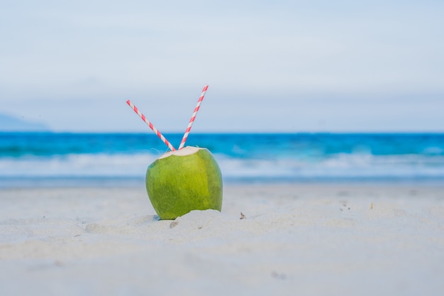 Coconut with straw in the sand on the beach.