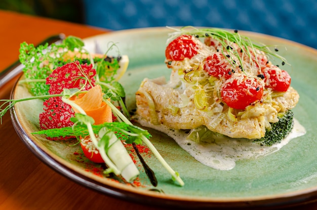 Cod fillet with tomatoes cherry and cheese, served with vegetables and micro greens. Close up