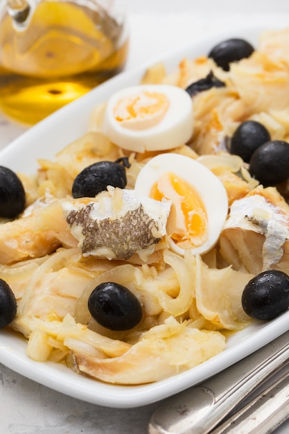 Cod fish with onion, olives, eggs and olive oil on dish on ceramic