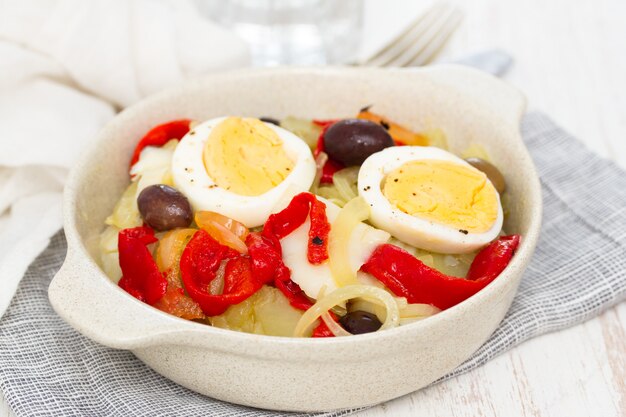 Cod fish with potato, red pepper, egg and olives on plate