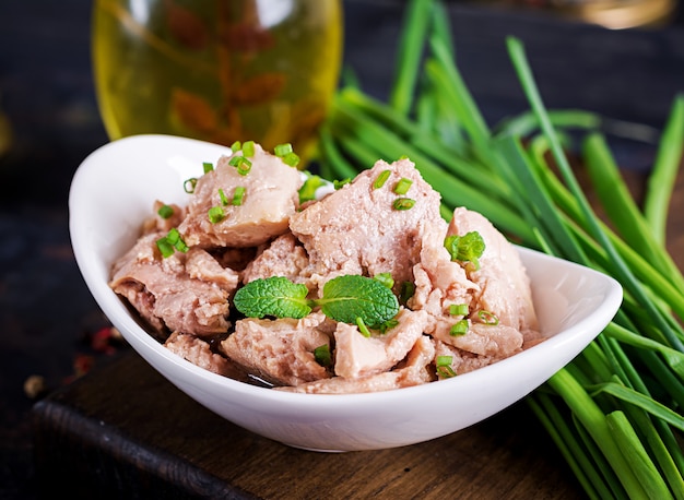 Cod liver with green onion in oil on plate.