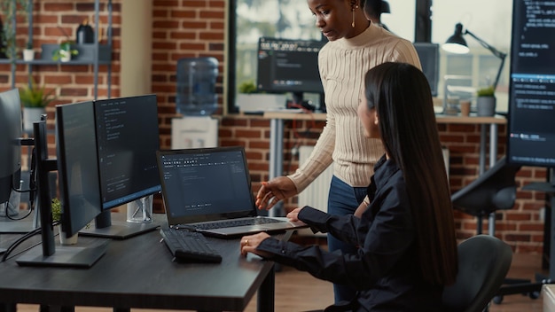 Coder holding laptop with coding interface entering software development agency office sitting down at desk meeting coworker. Programer getting inside it company to meet colleague for group project.