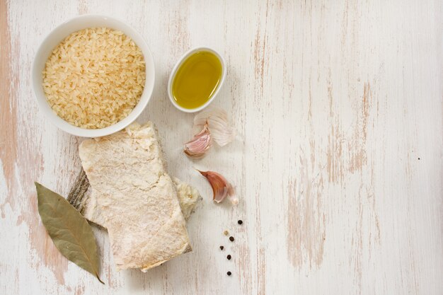 Merluzzo con riso, olio d'oliva e aglio su superficie di legno bianca