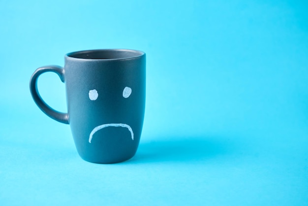 A coffe cup with a sad face on a plain blue background Blue Monday concept