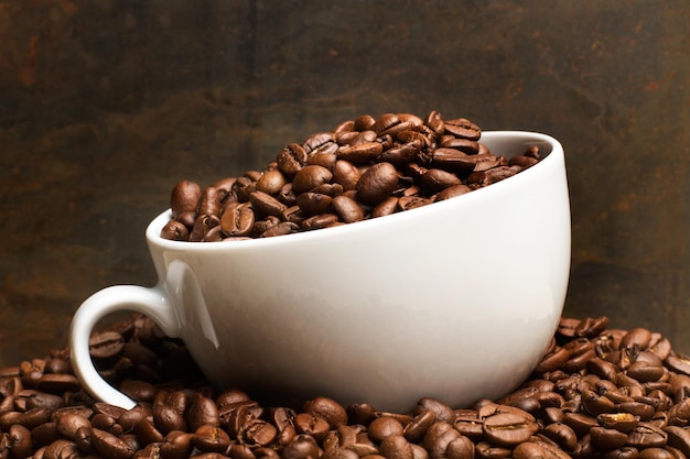 Coffe grains in a white cup and on a heap of coffee beans