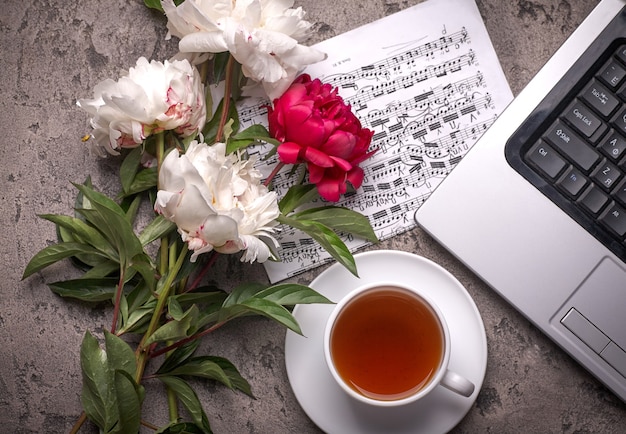 Coffe, peonies and laptop on grey vintage background