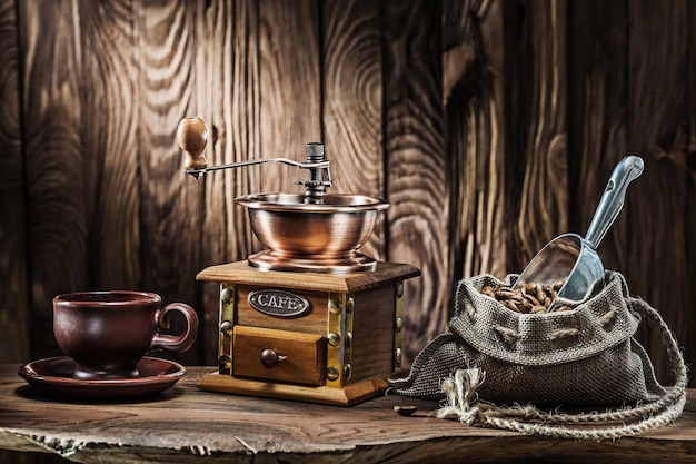 Coffee accessories brown clay cup vintage wooden mill and sack\
with beans scoop on old wood background