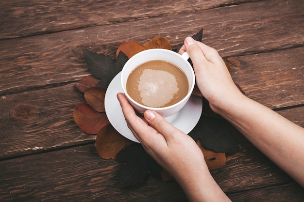 coffee and autumn leaves and hands on wooden background