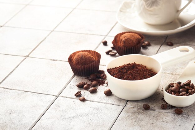 Coffee background Measuring spoons with ground coffee beans cup and sweet chocolate truffles on old tile cracked table background Food background Top view with space for your text