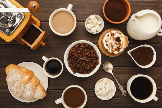 Coffee background. Top view on cups of various kinds of coffee, ground beans, milk, vintage grinder and sweet desserts on rustic wooden table