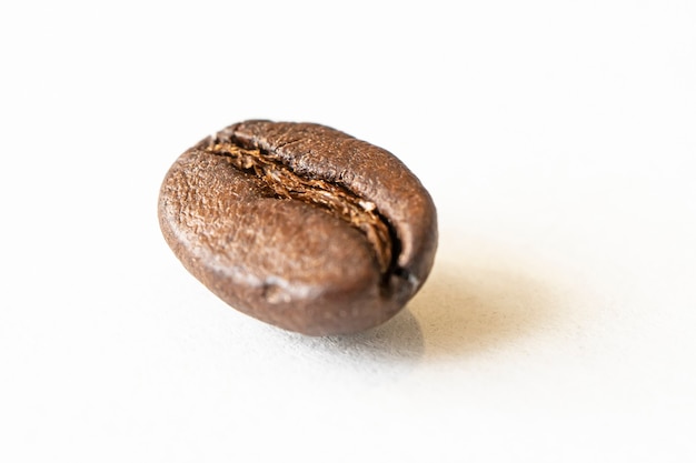 Foto chicco di caffè su sfondo bianco. una foto macro di chicchi di caffè marroni fritti sul tavolo bianco.