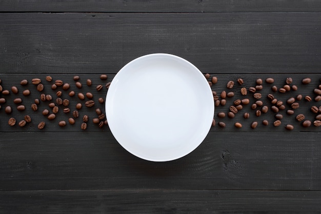 Coffee bean and white dish on black wooden. top view