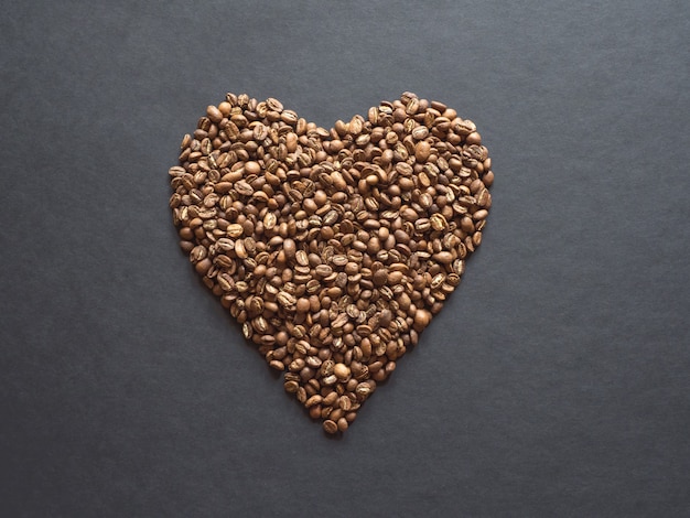 Coffee beans are laid out in the shape of a heart on a black table.