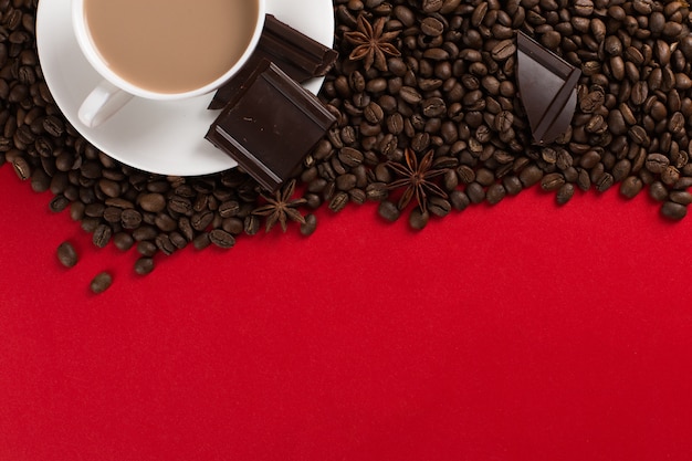 Coffee beans are scattered on a red paper  and a white cup, chocolate, , commercial copyspace.