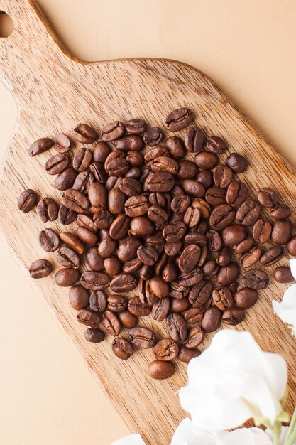 Coffee beans are scattered on a wooden board on a brown background. Vertical photo.