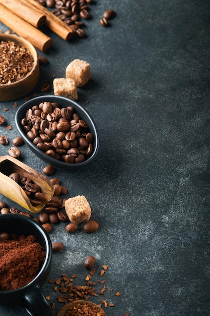 Coffee beans background roasted coffee concept with differents\
types of beans and cinnamon sticks on dark black stone background\
top view coffee concept mock up