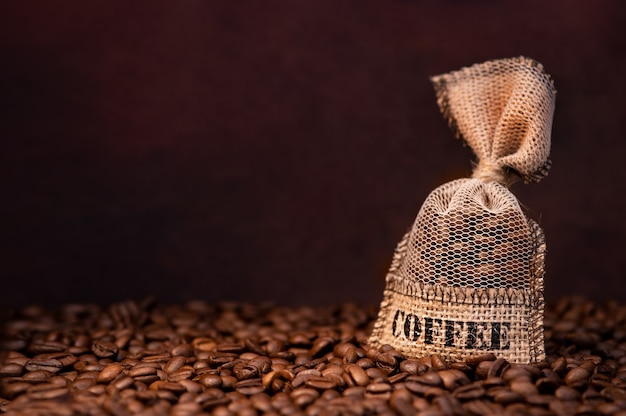 Chicchi di caffè in borsa su sfondo scuro con copia spazio. chicchi di caffè tostati freschi nel sacco di iuta.