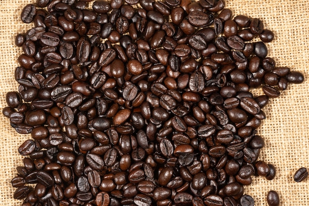 Coffee beans on brown linen fabric background. Roasted coffee beans texture, used as a background. Flat lay, top view, copy space. 