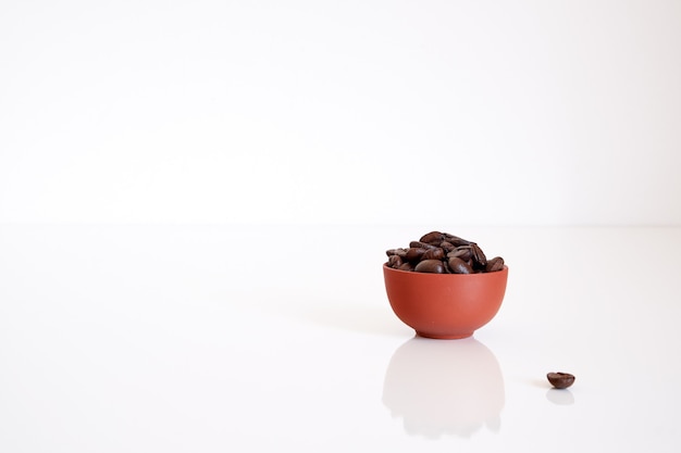 Foto chicchi di caffè in una tazza di argilla su sfondo bianco