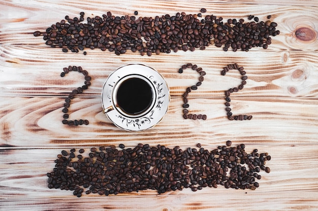 Foto chicchi di caffè, tazza di caffè e nome del chicco di caffè 2022 su uno sfondo di legno. concetto di natale e capodanno