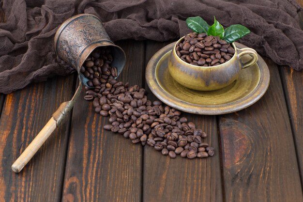 Chicchi di caffè in una tazza e una caffettiera su un tavolo di legno