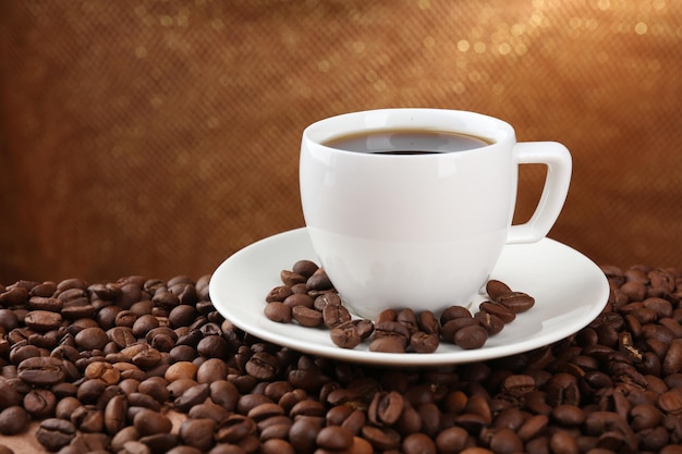 Coffee beans and cup of coffee on table on brown background