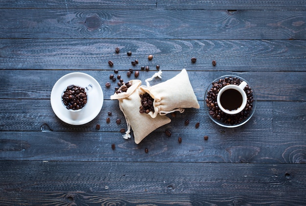 Coffee beans and cup of coffee with other components on different wooden surface. 