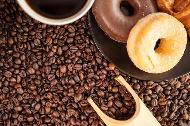 Coffee beans, donut and a cup of coffee in close up photo