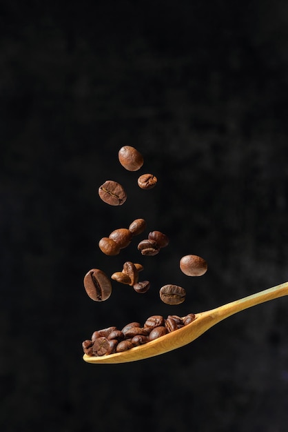 Coffee beans dropping on wood spoon on dark background