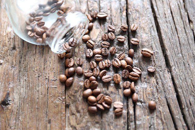 Кофейные зерна падают из стеклянной кофейной банки на деревянный текстурированный стол