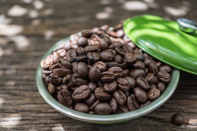 Coffee beans in green bowl on old wood background with sunlight