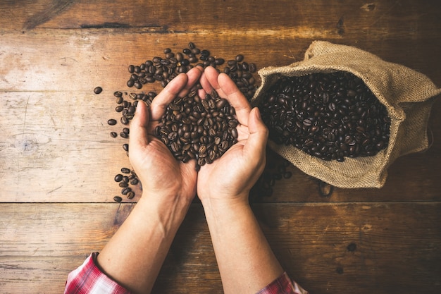 Coffee beans in hands on wooden background