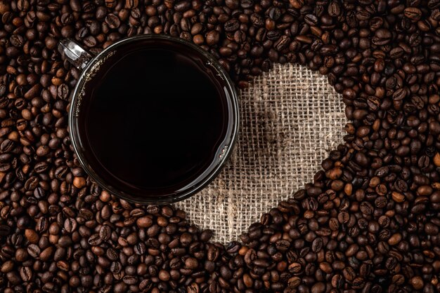 Coffee beans heart and cup of coffee on linen background.