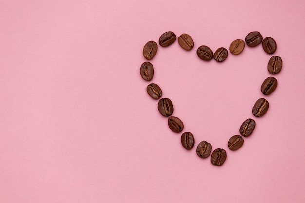 Coffee beans in heart shape on pink background. Copy spase