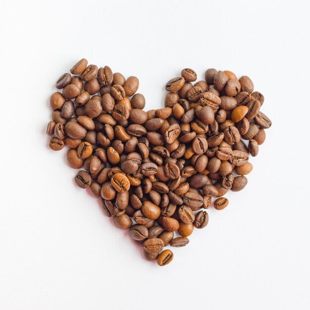 Coffee beans in heart shape on white surface